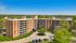 Impressive aerial view of a modern apartment building with spacious balconies, surrounded by lush greenery and ample parking in a serene neighborhood.