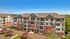 Charming multi-story apartment complex with modern architecture, featuring spacious balconies and surrounded by lush greenery and vibrant flowering trees.