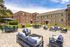 Charming apartment complex exterior featuring spacious outdoor patio with comfortable seating, umbrellas, and a grill, perfect for relaxation and entertaining.