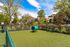 Charming outdoor space featuring a fenced green area with a playful tunnel, ideal for pets, surrounded by lush trees and picturesque residential buildings.