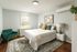 Inviting bedroom with elegant decor, featuring a plush bed, cozy armchair, and stylish floral artwork under ample natural light.