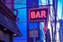 Vibrant urban street view with a glowing neon bar sign against a modern blue glass building backdrop.