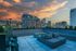 Stunning rooftop lounge with modern fire pit and cozy seating, offering panoramic city views at sunset.