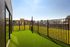 Charming urban balcony with lush green artificial grass, surrounded by sleek black railing, offering picturesque city views.