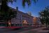 Elegant urban street view at dusk featuring a historic theater building glowing with bright marquee lights, surrounded by lush trees and bustling city life.