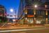 Vibrant cityscape with modern apartment building illuminated at dusk, featuring convenient access to retail stores and public transit.