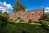 Charming brick apartment building surrounded by lush greenery and a welcoming landscaped path, perfect for peaceful living.