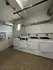 Modern laundry room with a row of white washing machines in a well-lit space featuring utility pipes and tiled flooring.