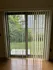 Inviting sliding glass door with vertical blinds offering a serene garden view, perfect for natural light and indoor-outdoor living.