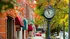Charming downtown street scene with vintage clock, vibrant autumn leaves, and cozy brick buildings featuring colorful awnings.