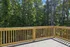 Charming sunlit balcony with a sturdy wooden railing overlooking a lush green forest, perfect for relaxing and enjoying nature.