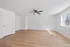 Bright and airy room with modern ceiling fan, pristine white walls, and stylish hardwood floors illuminated by natural light from a large window.