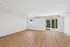 Bright, spacious room with light wood laminate flooring, featuring large windows and a sliding glass door opening to a serene outdoor view.