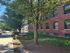 Charming brick apartment building with lush trees and a serene picnic area, perfect for outdoor relaxation.