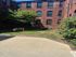 Charming brick apartment building with lush courtyard garden, featuring vibrant flowers and a mature tree.