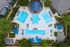 Aerial view of a luxurious community pool area featuring multiple sparkling blue swimming pools surrounded by comfortable lounge chairs and shaded seating areas amidst lush greenery.