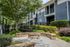 Charming apartment exterior with stylish blue facade, lush greenery, and inviting stone seating surrounding a fire pit.