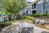 Charming outdoor patio area with a cozy fire pit, surrounded by lush greenery and modern grilling stations at a stylish apartment complex.