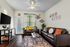 Charming living room with cozy dark leather sofas, vibrant decorative pillows, and a modern ceiling fan, featuring stylish wall art and lush green plants for a touch of nature.