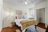 Elegant bedroom with warm wooden flooring, inviting bed adorned with soft pillows and a textured throw, complemented by cozy lighting and stylish macram&eacute; wall decor.