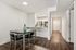 Bright and modern dining area with elegant dark wood flooring, adjacent to a sleek kitchen featuring stainless steel appliances and a spacious countertop.