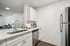 Modern kitchen with sleek white cabinetry, stainless steel appliances, and elegant countertop, seamlessly leading into a cozy living area.