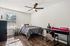 Bright and airy bedroom showcasing modern decor, featuring a cozy bed with elegant bedding, sleek black desk, and stylish ceiling fan on warm wooden flooring.