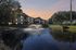 Charming apartment complex with beautiful pond and fountain, set against a serene sunset backdrop.
