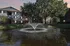 Charming apartment complex with a serene pond and elegant fountain, surrounded by lush greenery and vibrant exteriors.