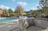 Inviting poolside view with stainless steel outdoor kitchen, surrounded by lush palm trees and clear blue skies.