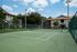Inviting apartment complex featuring a modern tennis court surrounded by lush greenery and elegant buildings under a bright blue sky.
