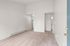 Bright and spacious living area with plush carpet and high ceiling, offering an open view into a cozy kitchen with a white refrigerator.
