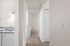 Bright apartment hallway with cozy carpet leading to bedrooms and a glimpse of a modern kitchen with a sleek sink and lighting.