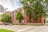 Charming urban apartment building with classic red brick facade, surrounded by lush greenery on a quiet street corner.