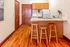 Charming kitchen nook with rich wooden flooring, tall bar stools, sleek countertop, and compact appliances.