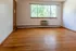 Bright living room with hardwood floors and large window providing natural light and a view of lush greenery.