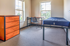 Bright and inviting bedroom with a modern desk, comfortable bed, and stylish dresser, bathed in natural light from large windows overlooking a lush view.