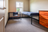 Inviting bedroom with natural light, featuring a cozy single bed, functional desk with chair, and sleek wooden dresser, ideal for a peaceful retreat.