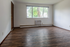 Bright and inviting living room with large window and elegant wood flooring, perfect for relaxation.