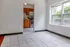 Bright and inviting apartment space with large windows, tiled flooring, and a view into a cozy kitchen with stylish wooden cabinets.