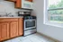 Charming kitchen with warm wooden cabinetry, modern stainless steel oven, and sunlit window view of lush greenery.