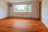 Bright and spacious room with stunning hardwood floors and a large window offering a serene view of lush greenery.