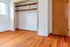Inviting empty room with polished hardwood flooring, a bright window, open closet space, and a warm wooden door.