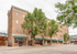 Charming brick apartment building with street-level shops, nestled amongst lush trees.