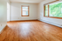 Bright and airy room with gleaming hardwood floors and large sunlit windows offering a serene view.
