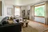 Elegant living room with large windows, cozy gray sectional sofa, chic wooden coffee table, and stylish shelving, exuding warm natural light and inviting ambiance.
