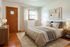Inviting bedroom with warm wooden accents, plush bedding, and a cozy rug, enhanced by natural light through large window.