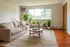 Bright and inviting living room with a cozy beige sofa, lush green plants, and a large window offering scenic outdoor views.