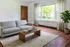 Inviting living room with a modern gray sofa, sleek wooden coffee table, and large window overlooking lush greenery, complemented by warm wood flooring and elegant curtains.