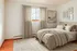 Elegant bedroom with plush bedding, soft beige tones, and tasteful wall art, accentuated by natural light through a large window and luxurious drapes.